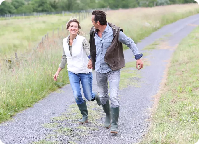 couple holding hands with wellies on running along a path