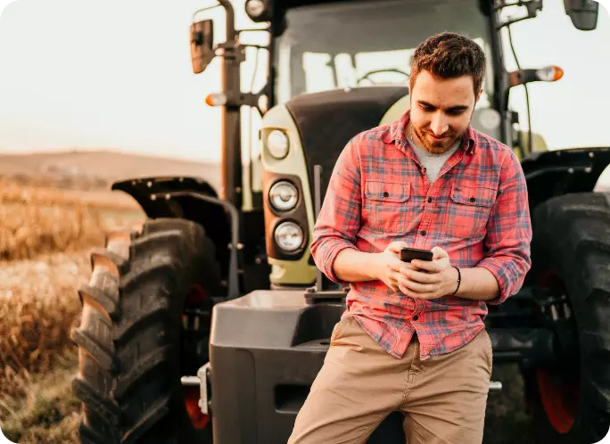 man messaging on his phone leaning on a tractor
